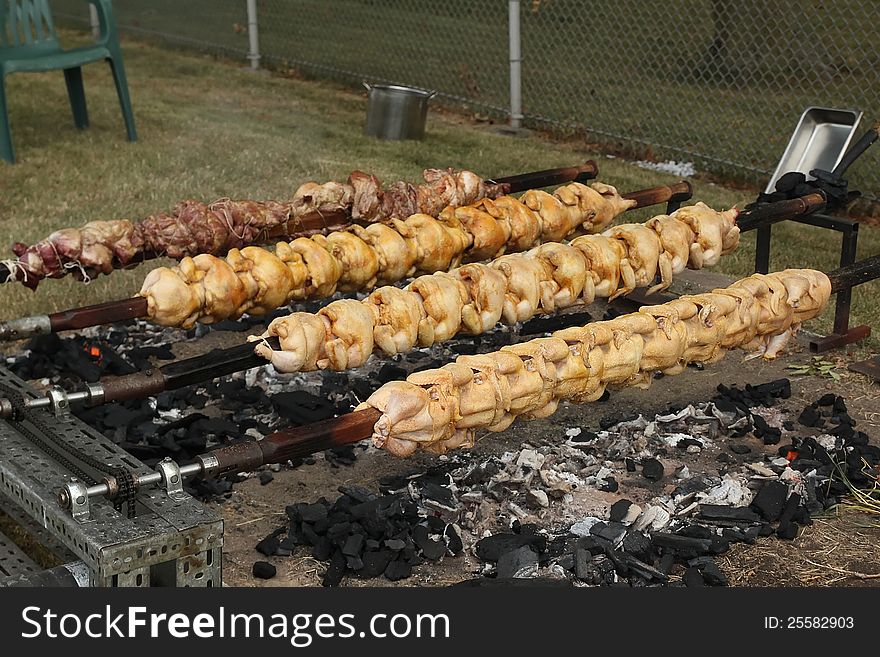 Roasted chicken and pork on outdoor spits. Charcoal burns under the spits, as the spits are continually turning to evenly cook the meat. A cookout for Independence Day in the USA, Photo taken July 4, 2012. Roasted chicken and pork on outdoor spits. Charcoal burns under the spits, as the spits are continually turning to evenly cook the meat. A cookout for Independence Day in the USA, Photo taken July 4, 2012.