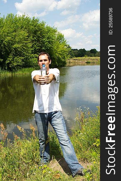 Young man stands near the river holding in his outstretched hands a bottle of water