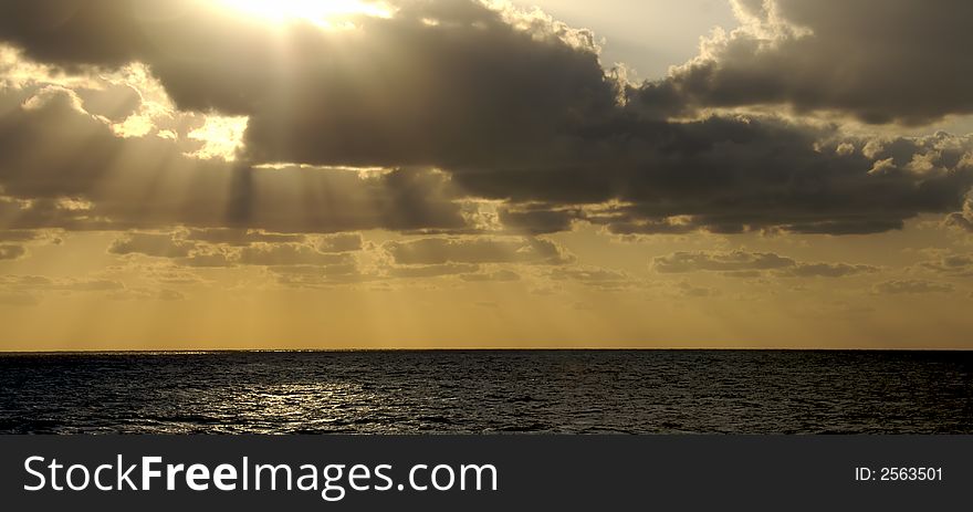 The golden rays of a sunset at sea bursts through the clouds. The golden rays of a sunset at sea bursts through the clouds