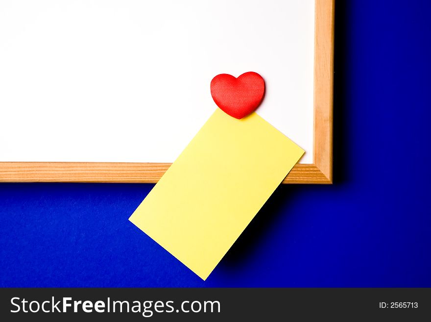 White-board with empty yellow post-it note and magnet in the form of a hart. White-board with empty yellow post-it note and magnet in the form of a hart