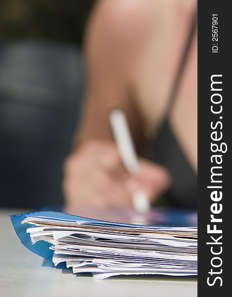 Stack of papers in front and pencil in hand in background. Stack of papers in front and pencil in hand in background