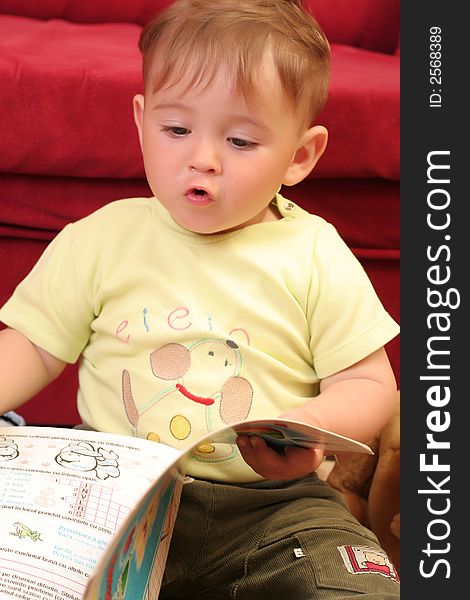 Expressive little blond baby boy gesticulate while reading a child book