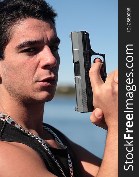 A young man, wearing a sleeveless shirt, holding a hand gun. (This image is part of a series). A young man, wearing a sleeveless shirt, holding a hand gun. (This image is part of a series)