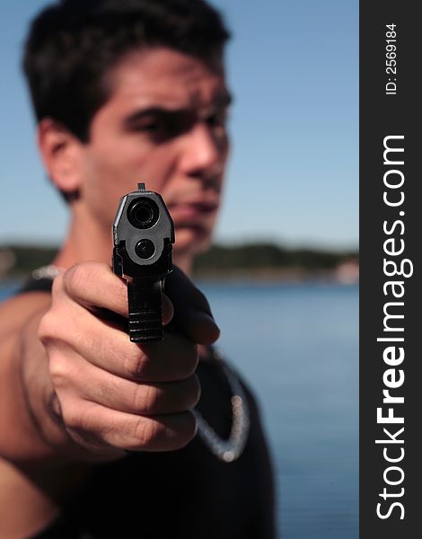 A young man, wearing a sleeveless shirt, holding a hand gun. (This image is part of a series). A young man, wearing a sleeveless shirt, holding a hand gun. (This image is part of a series)