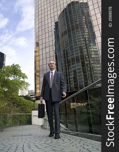 Businessman walking along a footbridge carrying his briefcase and with a city skyscraper behind him showing the reflection of another skyscraper. Businessman walking along a footbridge carrying his briefcase and with a city skyscraper behind him showing the reflection of another skyscraper