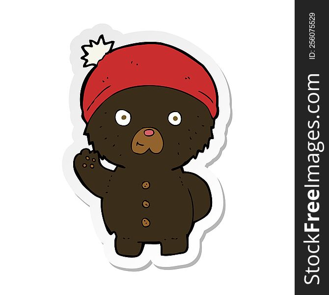 sticker of a cartoon waving black teddy bear in winter hat