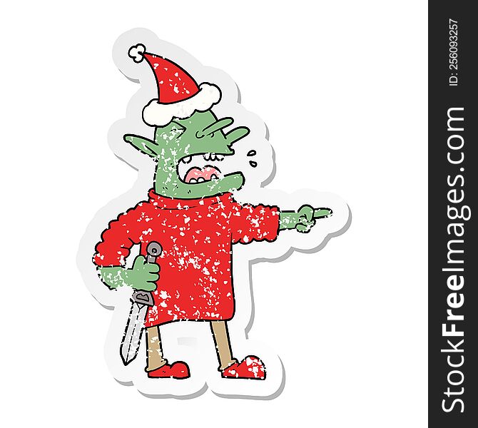 hand drawn distressed sticker cartoon of a goblin with knife wearing santa hat