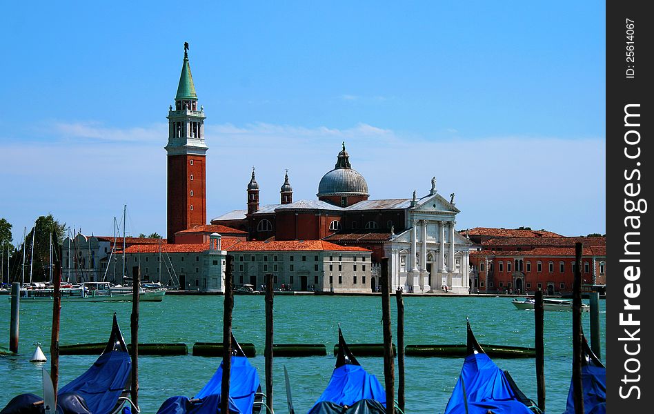 A fetching view across the sea towards the San Giorgio Maggiore island in Venice, Italy. In the foreground a row of traditional gondolas anchored in their pier.