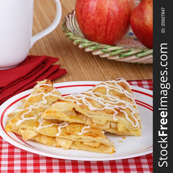 Two apple turnovers on a plate with apples in background