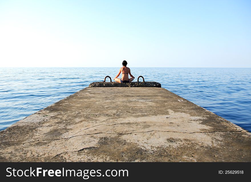 Beautiful adult woman sitting in lotus position on pier against sea. Beautiful adult woman sitting in lotus position on pier against sea