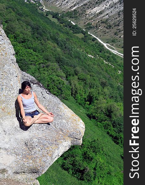 Beautiful adult woman sitting in lotus position on the rock above precipice. Beautiful adult woman sitting in lotus position on the rock above precipice