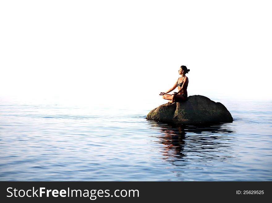 Svelte adult woman sitting in lotus position on the rock in the sea. Svelte adult woman sitting in lotus position on the rock in the sea