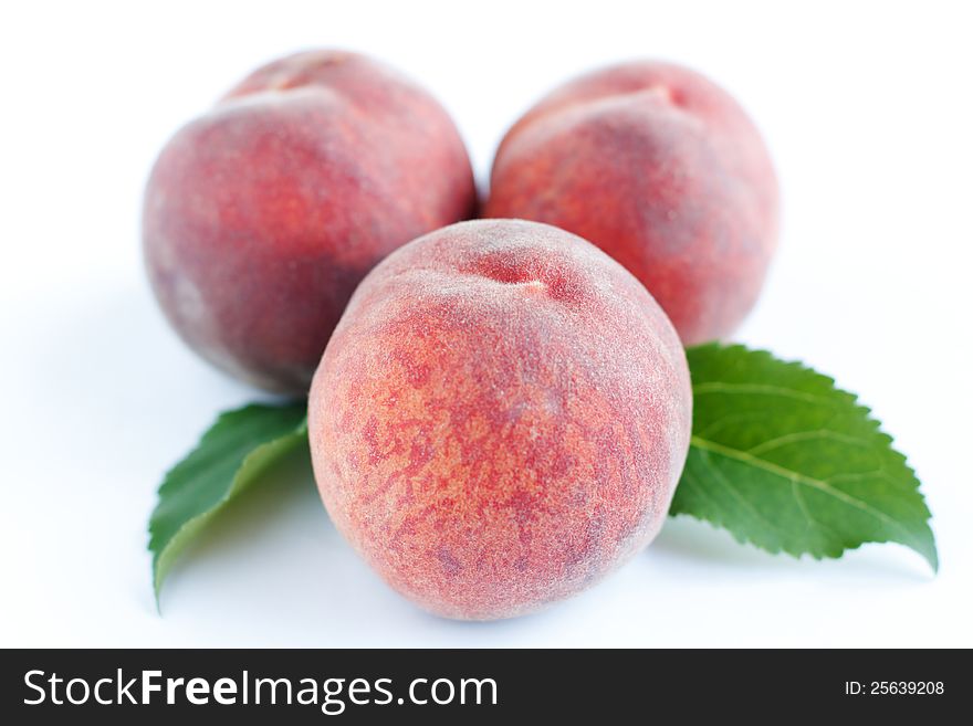 Three ripe pink peach and green leaves