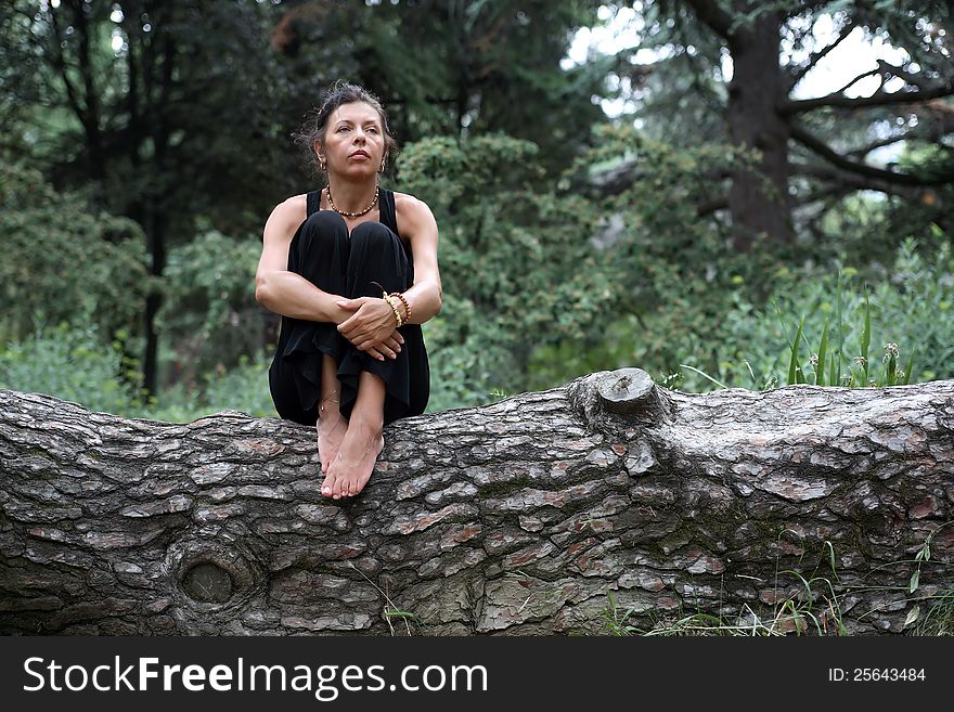 Portrait of strength attractive mature woman in black sitting on wooden log in forest. Portrait of strength attractive mature woman in black sitting on wooden log in forest