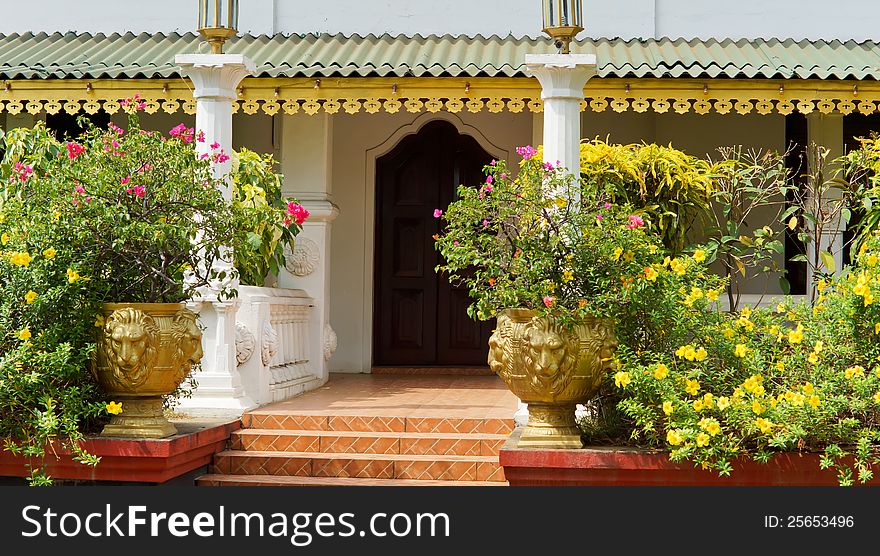 Entrance between pillars lined with flowerpots of colourful flowers to an ornate building with fretwork ornamentation