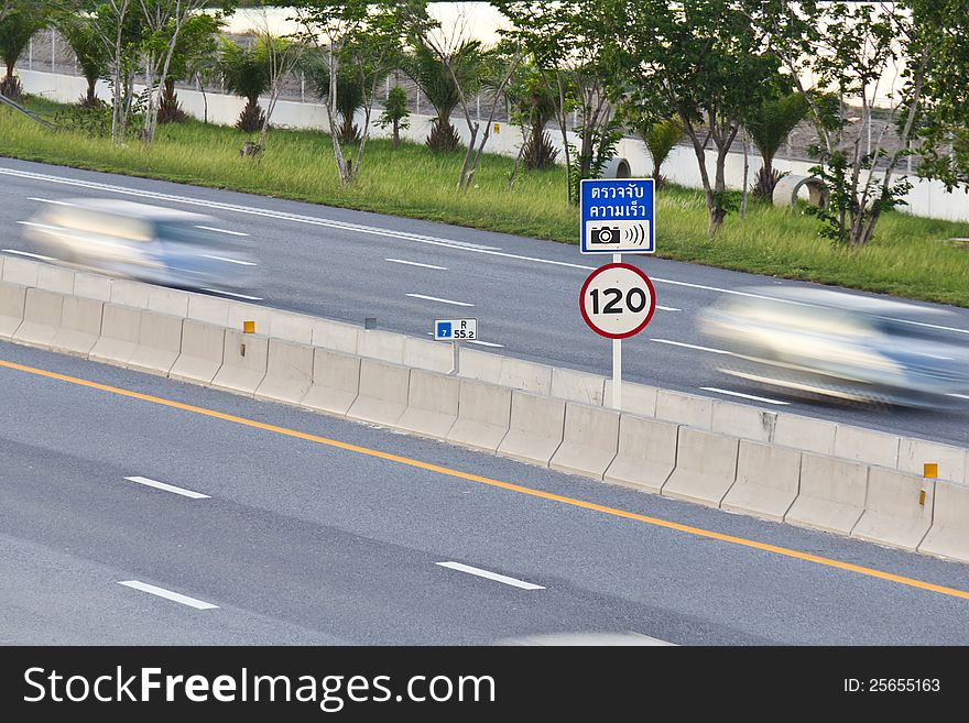 Speed limit (120 km/hour) and speed camera signpost on motor way with cars in motion. Speed limit (120 km/hour) and speed camera signpost on motor way with cars in motion