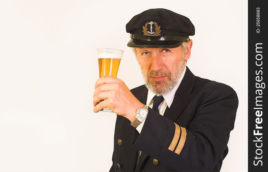 Horizontal image showing a matured, graying, unshaved seaman over 50 wearing a uniform with gold stripes on sleeves and mateâ€™s cap. His face is wrinkled, smiling, his eyes inviting. He keeps a glass of beer in his hand. Horizontal image showing a matured, graying, unshaved seaman over 50 wearing a uniform with gold stripes on sleeves and mateâ€™s cap. His face is wrinkled, smiling, his eyes inviting. He keeps a glass of beer in his hand.