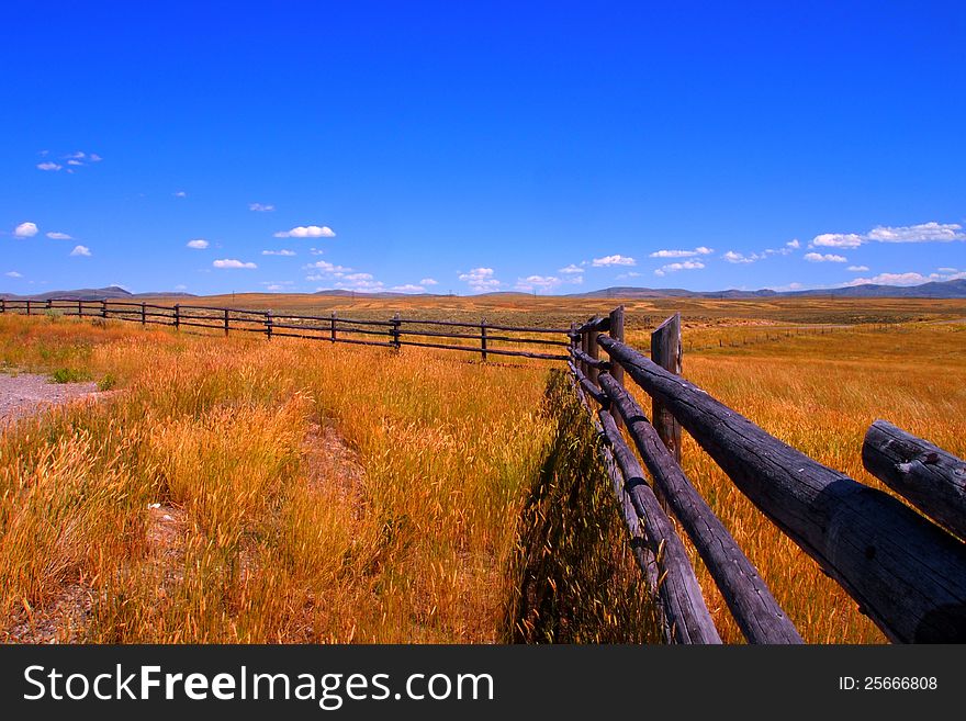 Grass field with wood fence and blue sky in Wyoming.