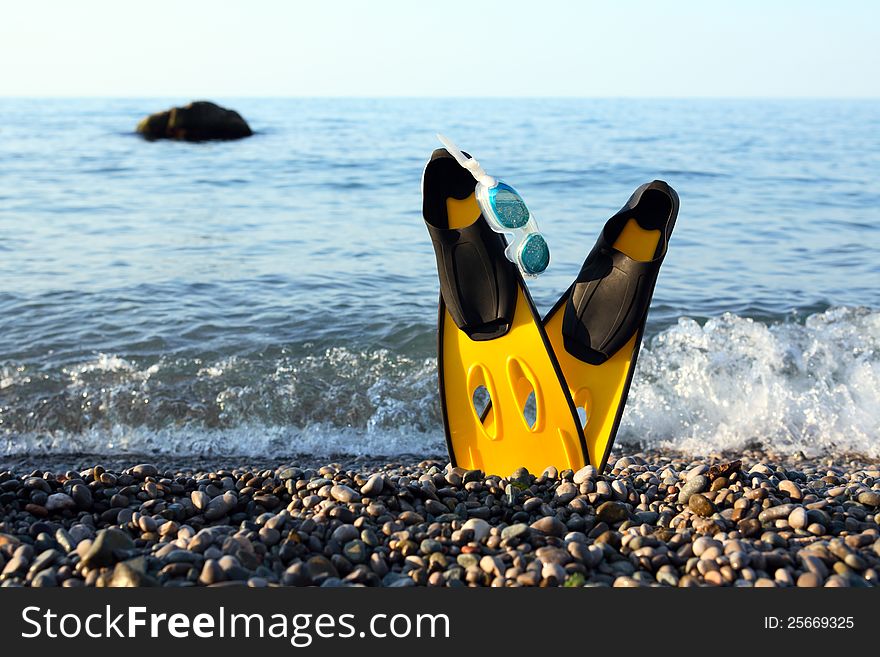 Diving concept. Pair of yellow flippers and goggles on seashore with free space for text. Diving concept. Pair of yellow flippers and goggles on seashore with free space for text