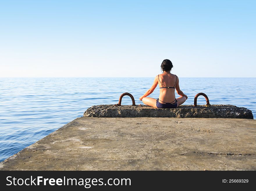 Svelte mature woman sitting on pier near sea and looking to horizon. Svelte mature woman sitting on pier near sea and looking to horizon