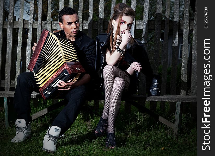 Couple young people - black men and white women sitting on bench against the fence. Accordion. Countryside. Serenade. Couple young people - black men and white women sitting on bench against the fence. Accordion. Countryside. Serenade