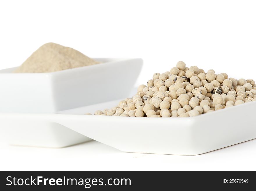 White pepper grain and powder on ceramic bowl