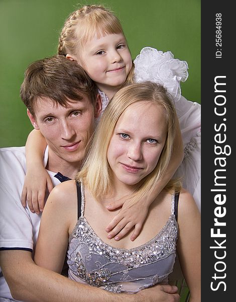 Young European family from three persons - mother, father and daughter. On a green background. Young European family from three persons - mother, father and daughter. On a green background.