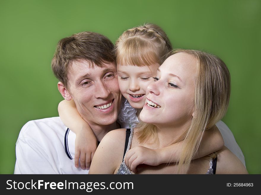 Young European family from three persons - mother, father and daughter. On a green background. Young European family from three persons - mother, father and daughter. On a green background.