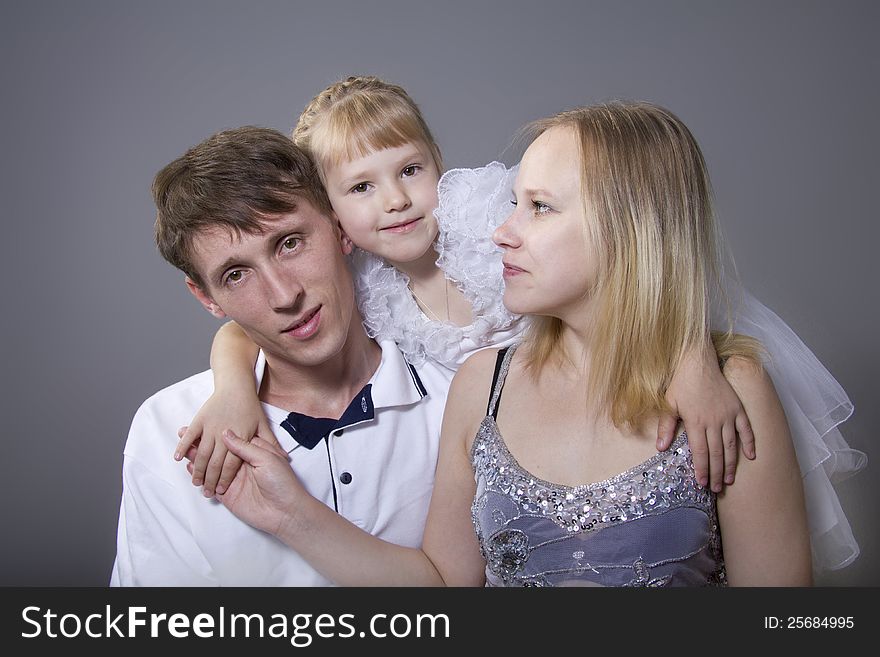 Young European family from three persons - mother, father and daughter. On a gray background. Young European family from three persons - mother, father and daughter. On a gray background