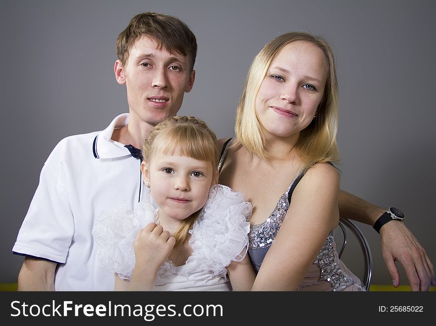Young European family from three persons - mother, father and daughter. On a gray background. Young European family from three persons - mother, father and daughter. On a gray background