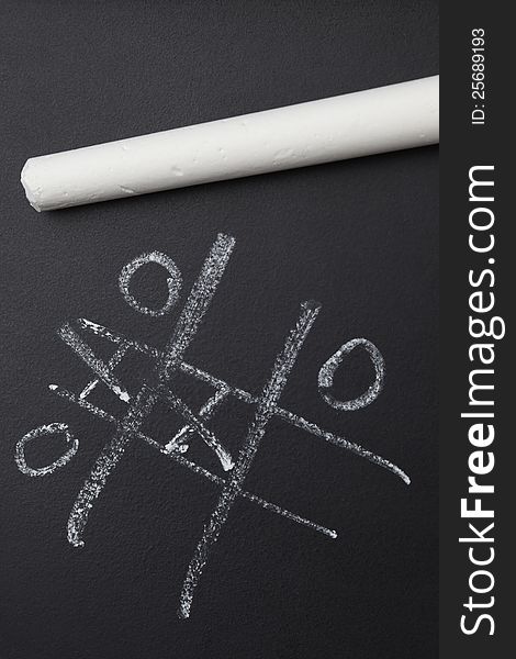 White chalk resting on black board with nought and crosses game. White chalk resting on black board with nought and crosses game