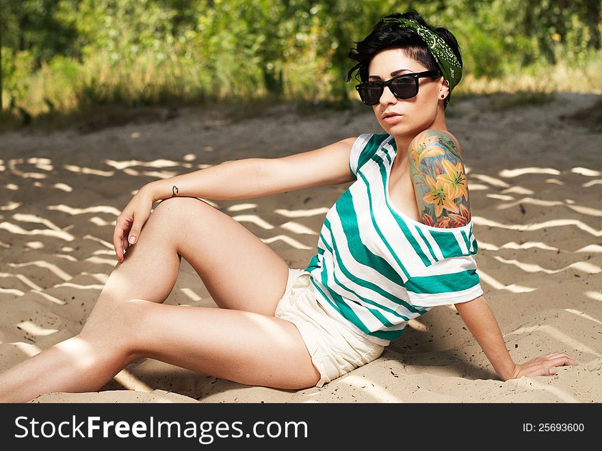 Pretty female model with tattoo and in sunglasses on the beach in the shade. Pretty female model with tattoo and in sunglasses on the beach in the shade