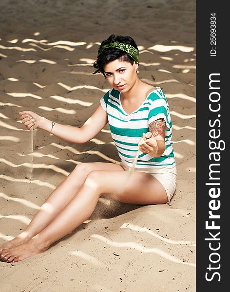 Pretty female model with tattoo on the beach in the shade pours sand. Pretty female model with tattoo on the beach in the shade pours sand