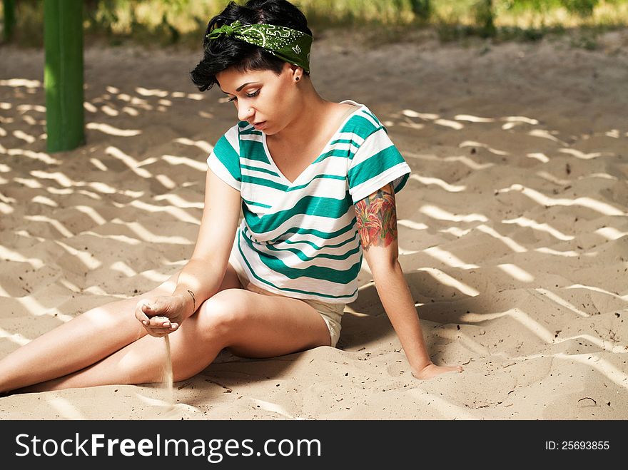 Pretty female model with tattoo on the beach in the shade pours sand. Pretty female model with tattoo on the beach in the shade pours sand