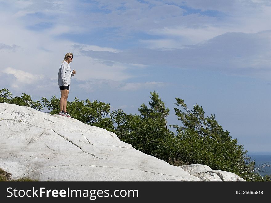 A lone female hiker stands on a rock ledge high above the surrounding landscape. A lone female hiker stands on a rock ledge high above the surrounding landscape.