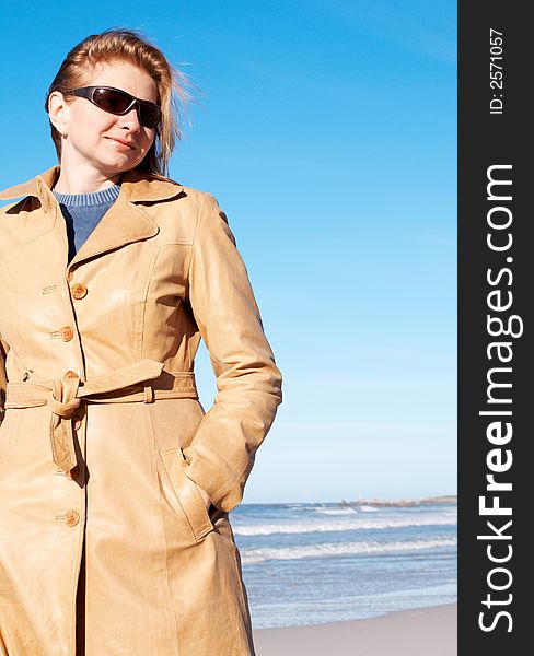 Blonde woman in a leather coat and sunglasses smiling. Blue sky in the background. Blonde woman in a leather coat and sunglasses smiling. Blue sky in the background.