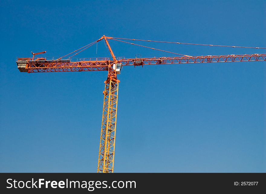 Construction crane in orange on a blue sky. Construction crane in orange on a blue sky