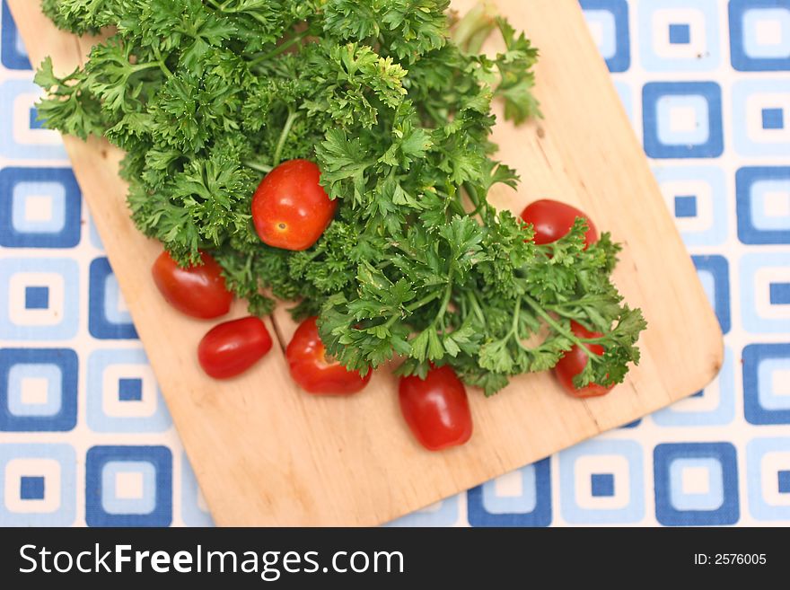 Bunch of parsley and cherry red tomatoes on wooden board and blue-squared mat. Bunch of parsley and cherry red tomatoes on wooden board and blue-squared mat.