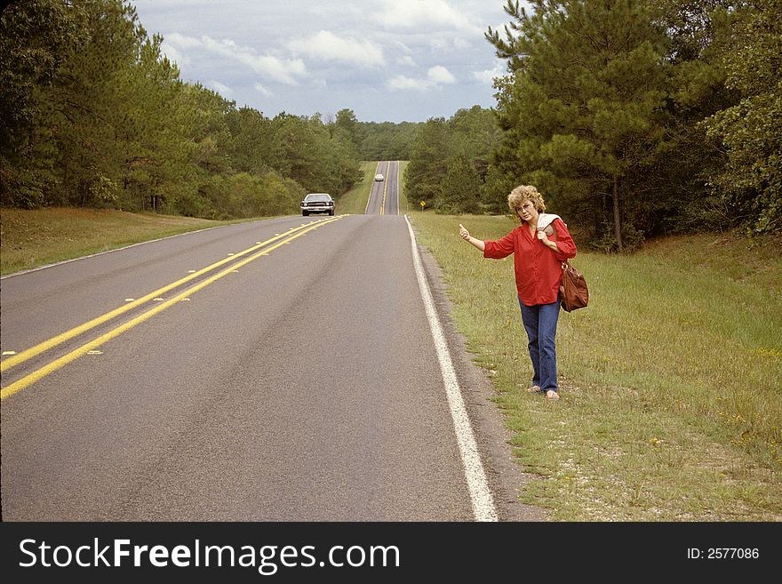 Woman standing beside highway with her thumb out indicating she wants a ride. Woman standing beside highway with her thumb out indicating she wants a ride