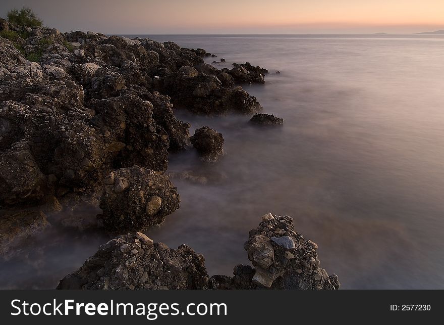 Image shows a serene rocky seascape right after sunset. Image shows a serene rocky seascape right after sunset