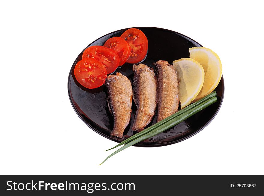 Small sprats on a black plate with lemon, tomatoes and green onions