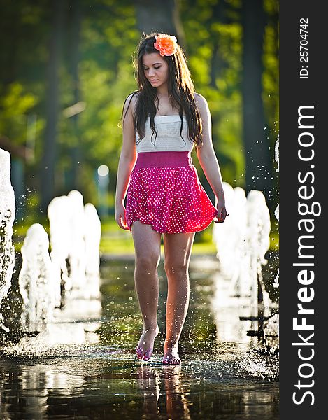 Young beautiful brunette girl wearing red skirt playing at outdoor water fountain in a hot day. Young beautiful brunette girl wearing red skirt playing at outdoor water fountain in a hot day