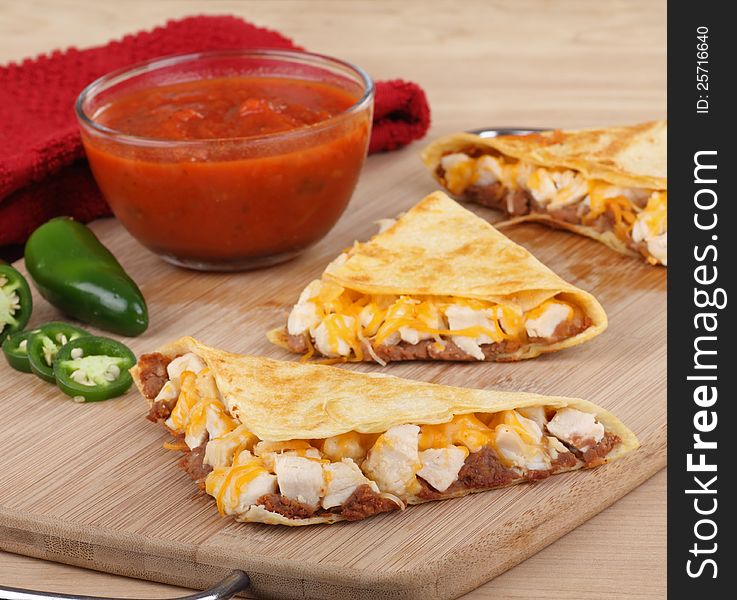Chicken quesadillas cut into wedges with salsa and pepper on a cutting board. Chicken quesadillas cut into wedges with salsa and pepper on a cutting board