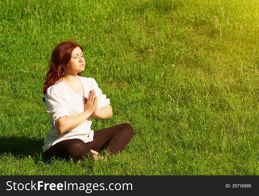 Young redhead woman practicing yoga lotus pose outdoors on the grass on the lawn in the park. Young redhead woman practicing yoga lotus pose outdoors on the grass on the lawn in the park