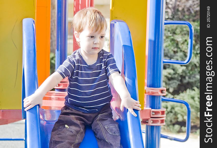 Small boy sitting on top the slide preparing to slide down. Small boy sitting on top the slide preparing to slide down.