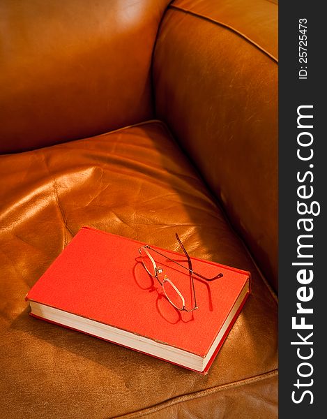 Comfy leather chair with red book and glasses, waiting for a reader. Comfy leather chair with red book and glasses, waiting for a reader