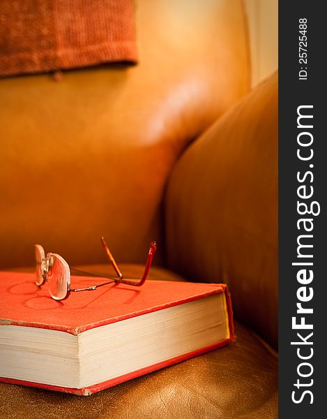 Comfy leather chair with red book and glasses, waiting for a reader. Comfy leather chair with red book and glasses, waiting for a reader