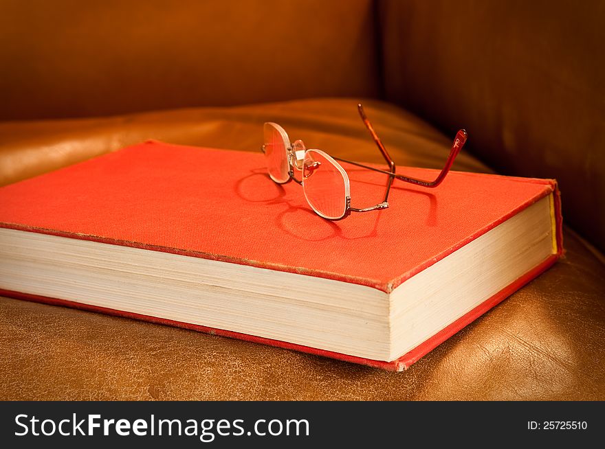 Comfy leather chair with red book and glasses, waiting for a reader. Comfy leather chair with red book and glasses, waiting for a reader