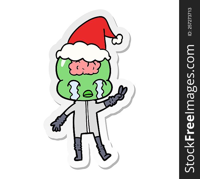 hand drawn sticker cartoon of a big brain alien crying and giving peace sign wearing santa hat