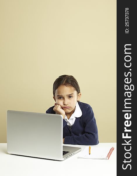Young girl using laptop on white desk with homework looking bored